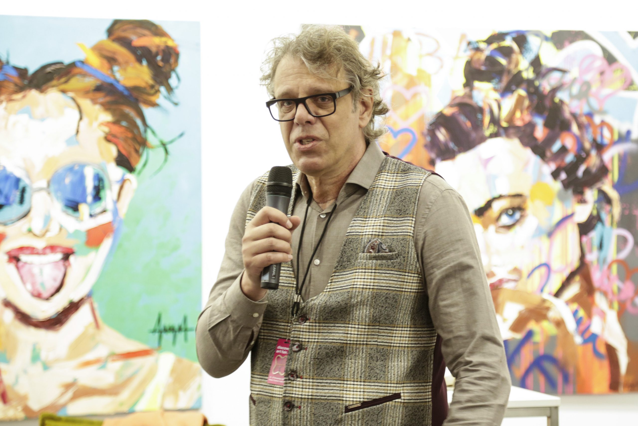 Gérard Margaritis director of the 30works gallery speaks at the art fair holding a mic to his mouth