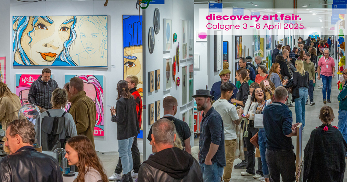 A picture of the Discovery Art Fair shows crowded aisles with numerous visitors visiting the various stands. A wide variety of artworks are on display at the stands, including paintings, sculptures and photographs.